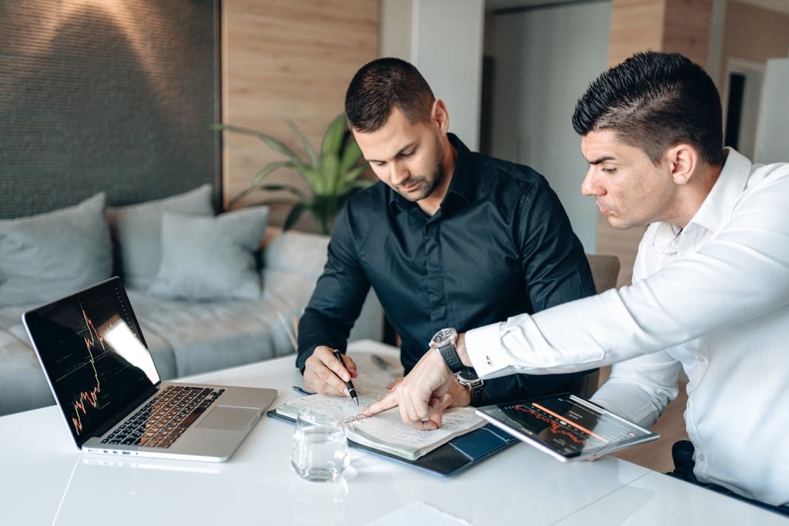kenson Investments | Future Market Trends: The Rise of Real-World Asset Tokenization and Global Digital Asset Adoption Two men discussing digital asset investment solutions with a laptop and a tablet displaying market data on a table.