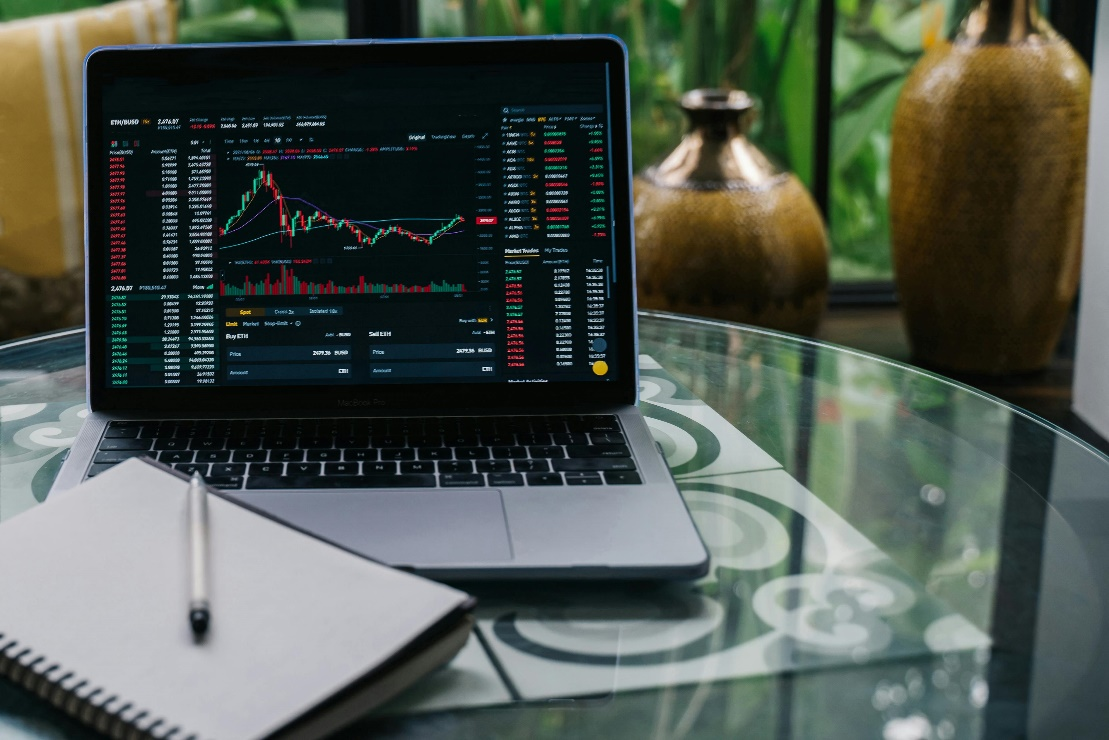 A laptop displaying a stock market chart with accompanying data on a glass table.