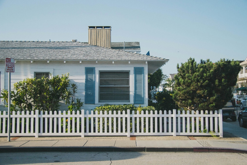  A small, white house with a blue window and a white picket fence.