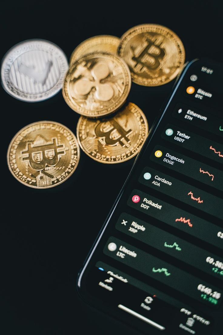 Various cryptocurrency coins and a phone showing a crypto trading app.