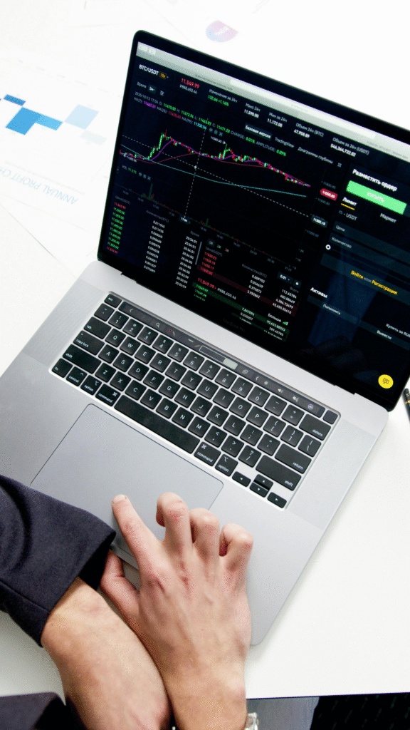 A person’s hand on a MacBook trackpad with a cryptocurrency exchange interface displayed on the screen.
