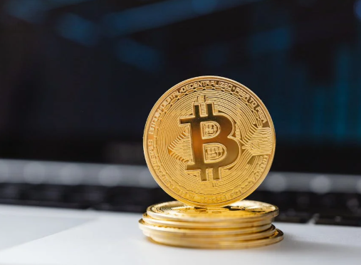 A stack of gold-colored physical Bitcoin tokens placed on a white surface in front of a blurred laptop keyboard.