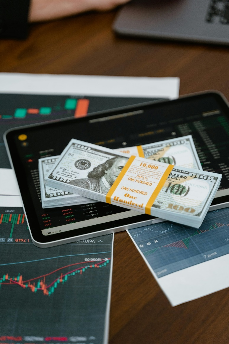 A tablet displaying financial charts and graphs, with stacks of US dollar bills.
