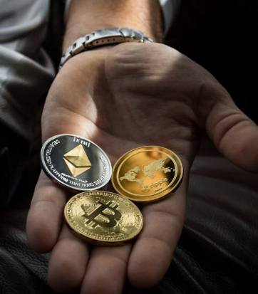 A person’s open hand holding three physical cryptocurrency tokens representing Ethereum, Bitcoin, and a world map design.