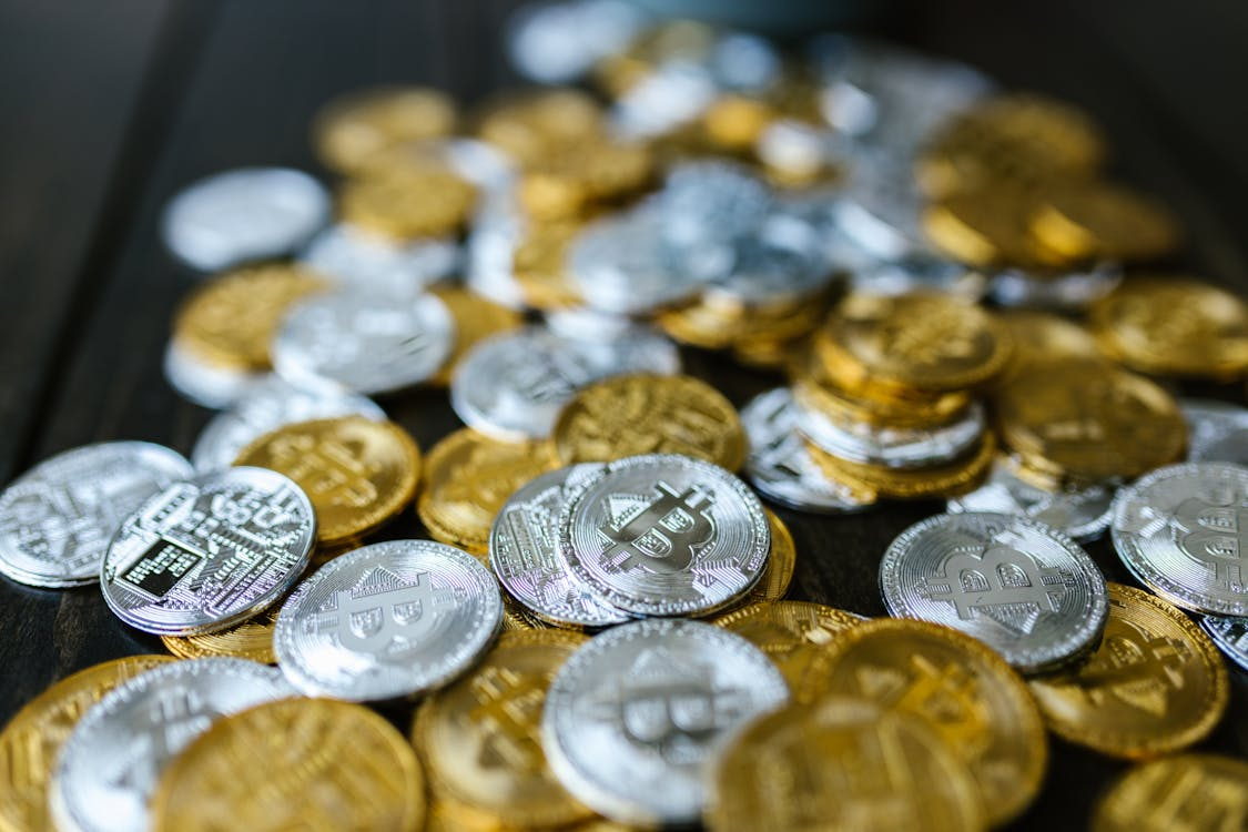 A scattered pile of silver and gold-colored physical Bitcoin tokens spread across a dark wooden surface.