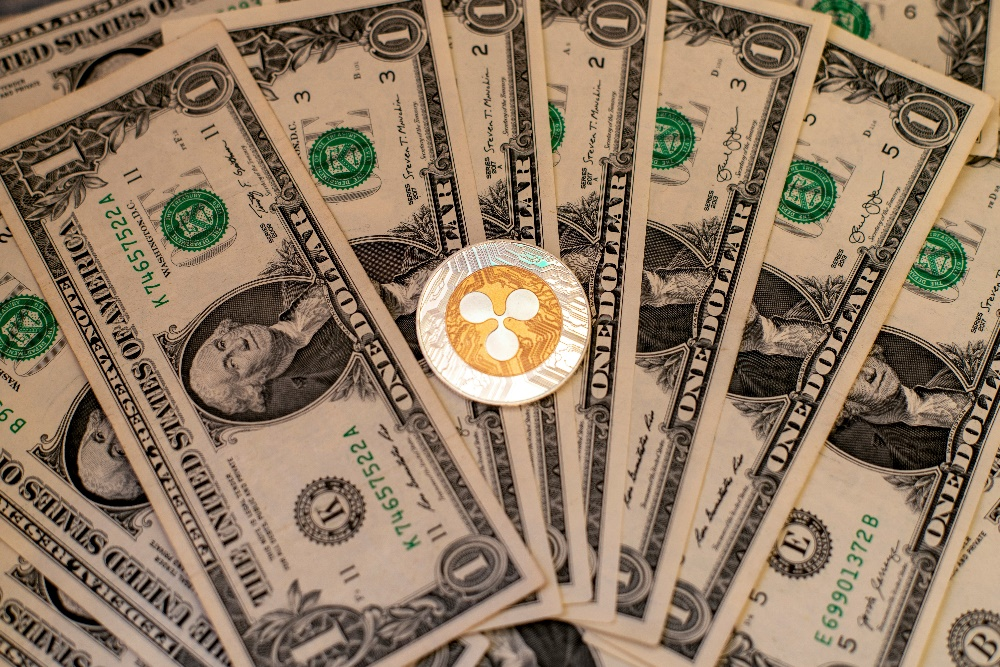 A single XRP cryptocurrency coin centrally placed on several US one-dollar bills.
